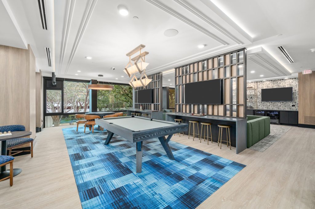 The Watt Lounge, with green sofas, yellow chairs, a shelf with various decorative items, and 3 flat screen tvs, a pool table and poker table.